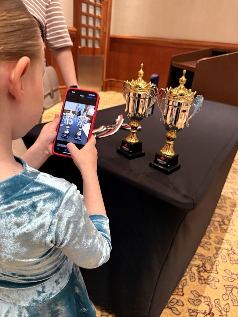 A young dancer taking a photo of trophies